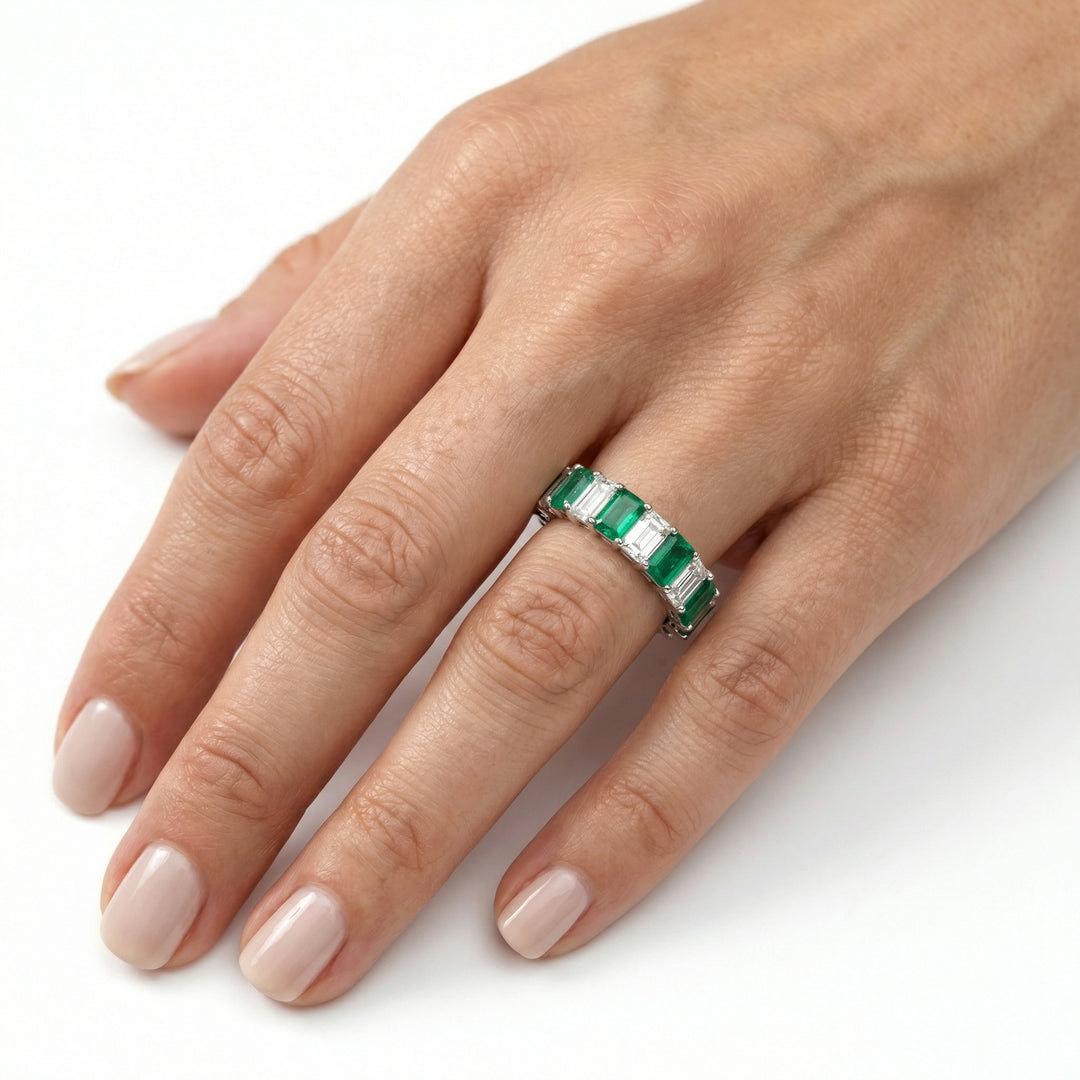 Platinum emerald cut eternity ring with alternating white diamonds and green emeralds on ring finger
